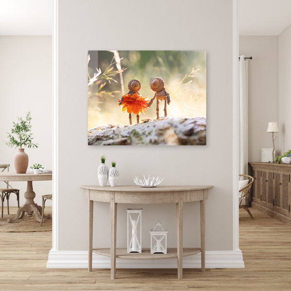 The photo of two Becorns holding hands as a metal print, mounted without a frame on a pale gray wall. The metal print faintly reflects an unseen plain wall. Underneath it is an accent table.