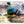 A male mallard duck biting at a Becorn in a small boat. The Becorn looks frightened. The duck and Becorn are blurry with movement.